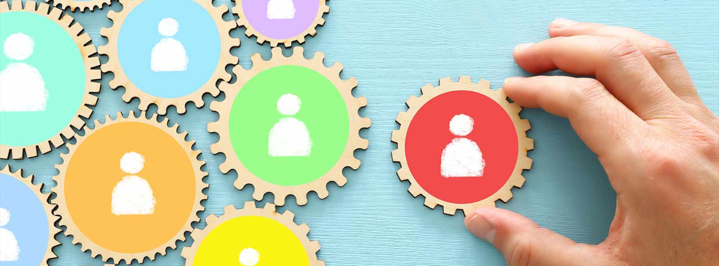 A hand placing colorful gears together with human shaped symbols on each one.